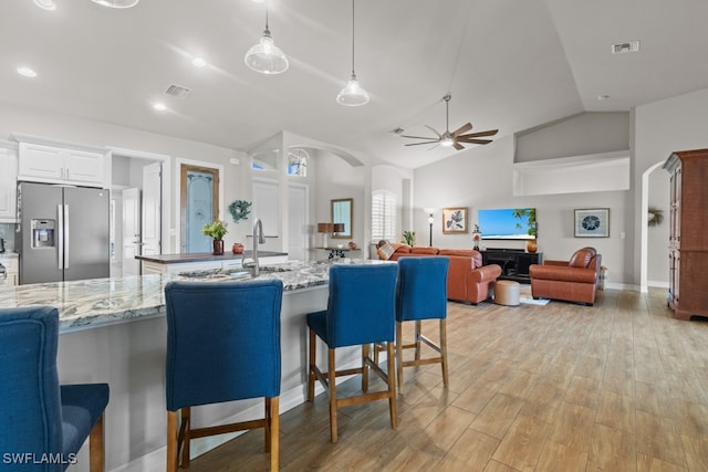 kitchen featuring white cabinets, hanging light fixtures, stainless steel fridge, ceiling fan, and a kitchen bar