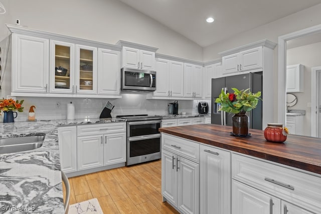 kitchen with vaulted ceiling, light hardwood / wood-style floors, stainless steel appliances, white cabinetry, and butcher block counters