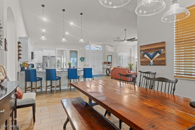 dining area featuring ceiling fan, sink, light wood-type flooring, and a towering ceiling