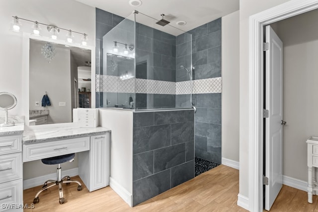 bathroom with tiled shower, vanity, and wood-type flooring