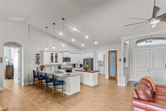 kitchen with white cabinets, light hardwood / wood-style flooring, stainless steel appliances, dark stone counters, and a kitchen island