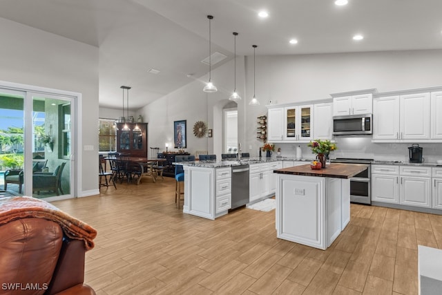 kitchen with high vaulted ceiling, decorative light fixtures, appliances with stainless steel finishes, and light hardwood / wood-style flooring