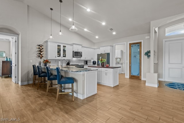 kitchen with kitchen peninsula, appliances with stainless steel finishes, white cabinetry, and light hardwood / wood-style floors