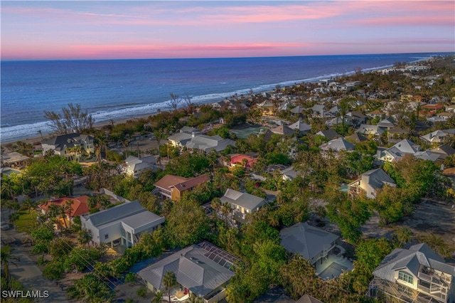 aerial view at dusk featuring a water view and a beach view