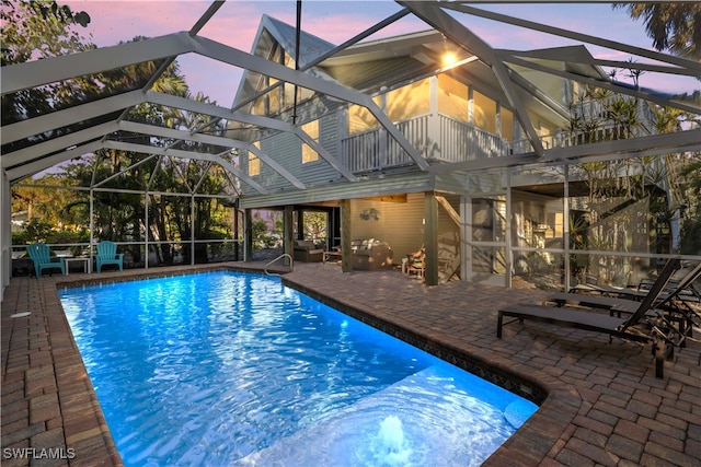 pool at dusk with glass enclosure and a patio area