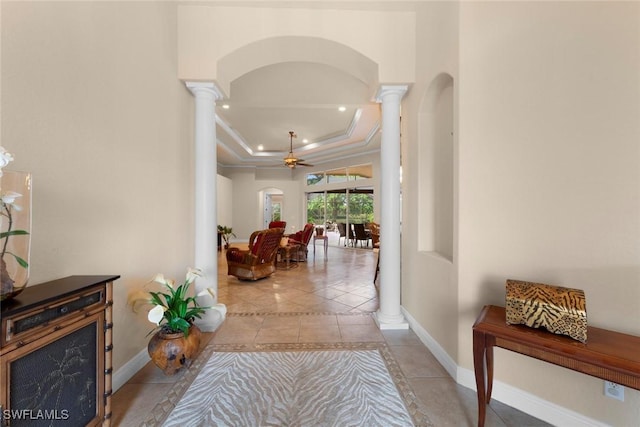 hallway featuring a raised ceiling, light tile patterned floors, ornamental molding, and decorative columns