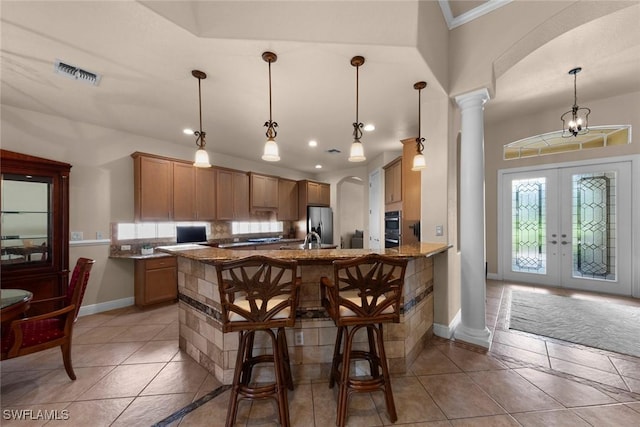 kitchen featuring pendant lighting, french doors, stone countertops, a breakfast bar area, and decorative columns