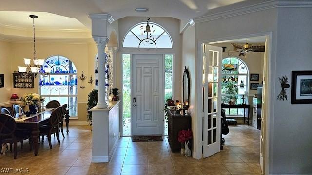 tiled entryway with ceiling fan with notable chandelier, decorative columns, and ornamental molding