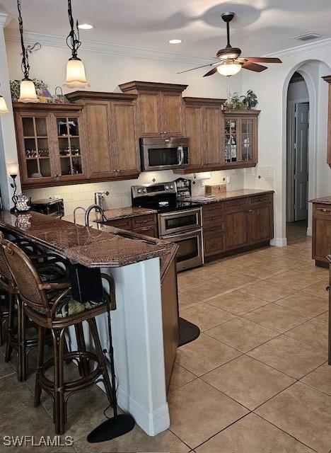 kitchen featuring hanging light fixtures, stainless steel appliances, dark stone countertops, decorative backsplash, and a breakfast bar