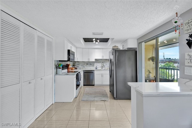 kitchen with decorative backsplash, white cabinetry, light tile patterned floors, stainless steel appliances, and a textured ceiling