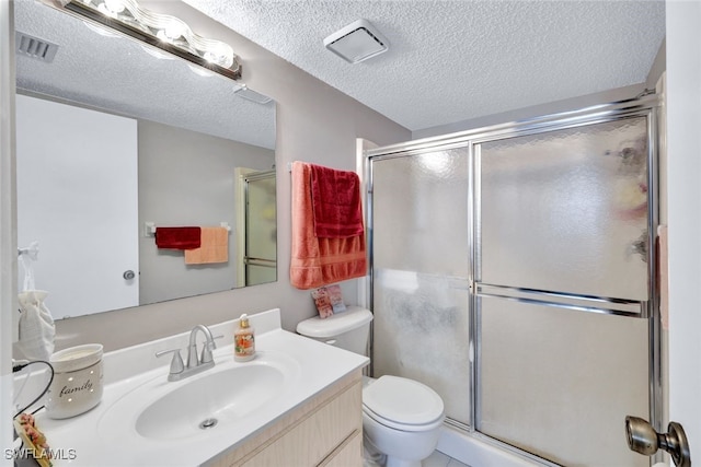 bathroom with a textured ceiling, a shower with door, vanity, and toilet