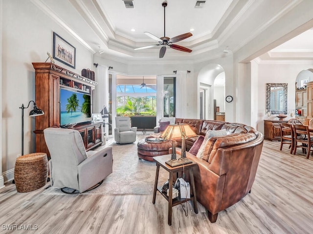 living room with ceiling fan, a tray ceiling, crown molding, and light hardwood / wood-style floors