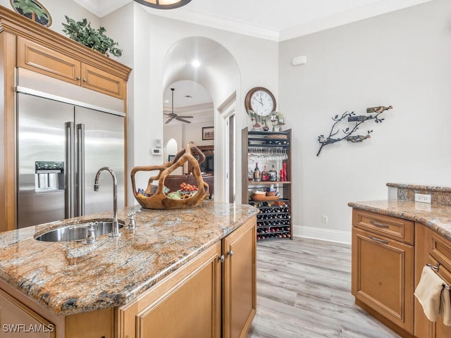 kitchen with stainless steel built in refrigerator, an island with sink, light hardwood / wood-style flooring, light stone countertops, and ceiling fan