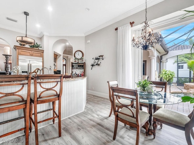 dining room featuring ornate columns, a chandelier, light hardwood / wood-style floors, and crown molding