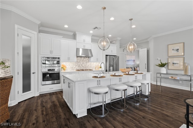 kitchen with appliances with stainless steel finishes, dark hardwood / wood-style flooring, white cabinetry, decorative light fixtures, and a kitchen island with sink