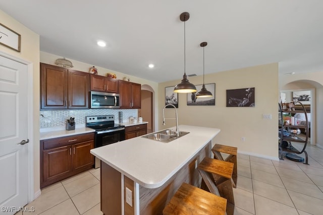 kitchen featuring appliances with stainless steel finishes, hanging light fixtures, a kitchen bar, a kitchen island with sink, and sink