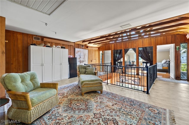 sitting room with wooden walls, beam ceiling, and light hardwood / wood-style flooring