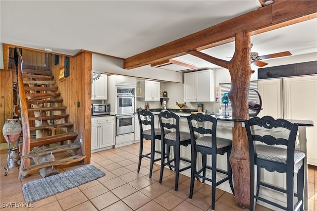 kitchen featuring white cabinets, beam ceiling, stainless steel appliances, light tile patterned floors, and ceiling fan