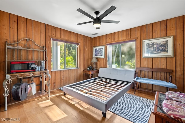 bedroom with ceiling fan, wood walls, and light hardwood / wood-style floors