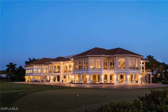 back house at dusk with a lawn and a balcony