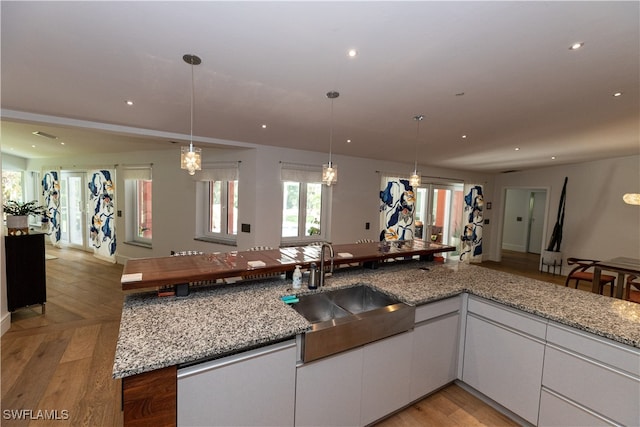 kitchen featuring light stone counters, white cabinets, light wood-type flooring, sink, and a notable chandelier