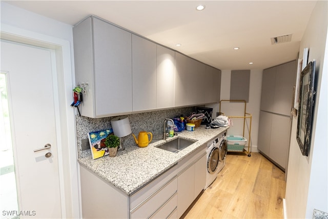 kitchen featuring sink, washing machine and clothes dryer, tasteful backsplash, light stone countertops, and light hardwood / wood-style floors