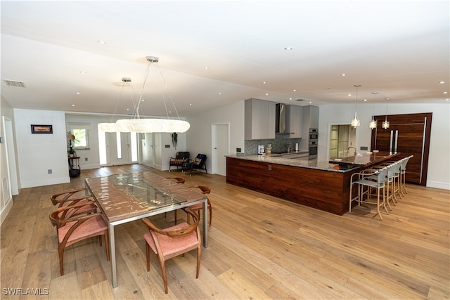 kitchen with light hardwood / wood-style floors, tasteful backsplash, wall chimney exhaust hood, light stone countertops, and a notable chandelier