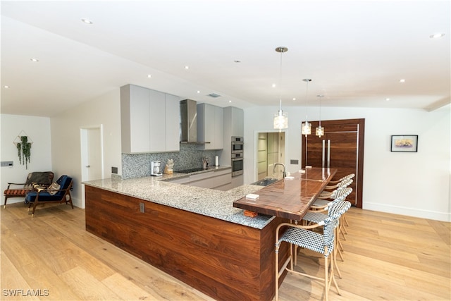 kitchen featuring pendant lighting, kitchen peninsula, wall chimney exhaust hood, black electric stovetop, and light hardwood / wood-style floors