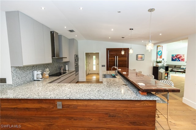 kitchen featuring black electric cooktop, light stone counters, lofted ceiling, light hardwood / wood-style flooring, and wall chimney range hood