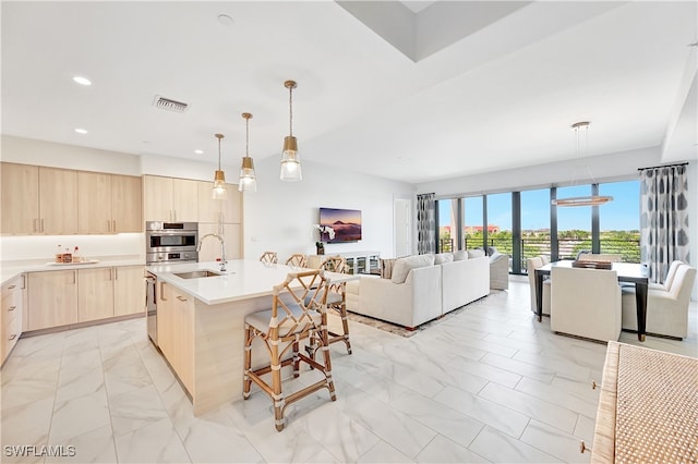 kitchen featuring sink, hanging light fixtures, a kitchen breakfast bar, a center island with sink, and light brown cabinetry