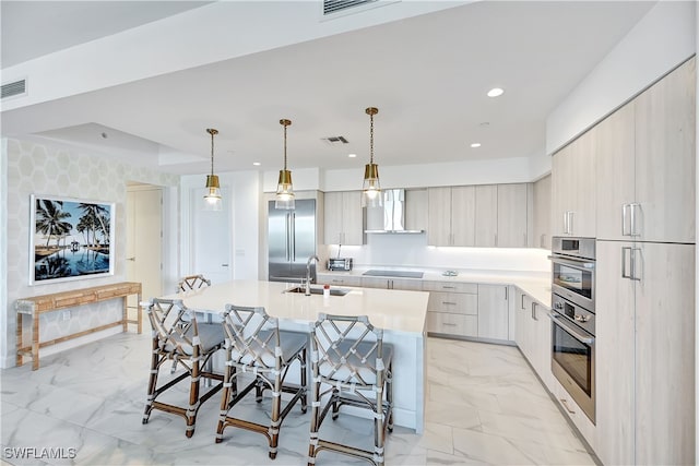 kitchen with stainless steel built in refrigerator, pendant lighting, sink, an island with sink, and wall chimney exhaust hood