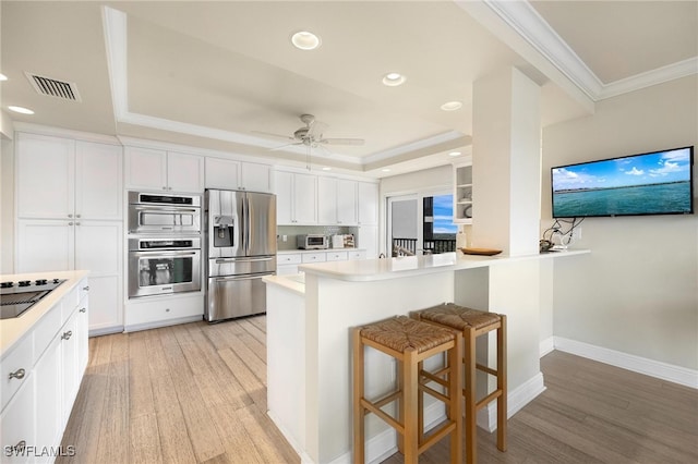 kitchen featuring a breakfast bar, white cabinets, crown molding, light wood-type flooring, and appliances with stainless steel finishes