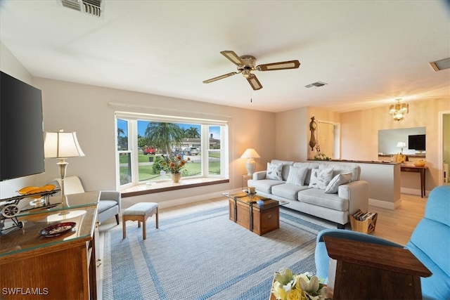 living room featuring ceiling fan with notable chandelier and light wood-type flooring