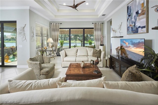 living room featuring ceiling fan, light tile patterned floors, a tray ceiling, ornamental molding, and a water view