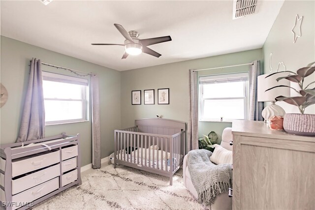 carpeted bedroom featuring multiple windows, a crib, and ceiling fan