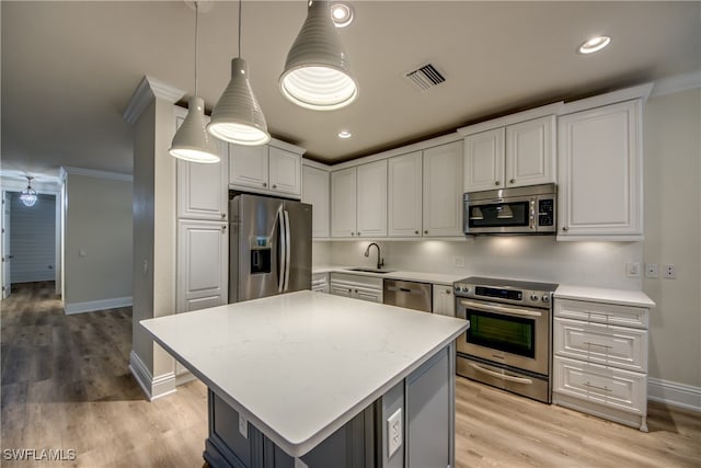 kitchen featuring white cabinets, hanging light fixtures, ornamental molding, appliances with stainless steel finishes, and a center island