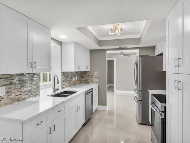 kitchen featuring appliances with stainless steel finishes, sink, white cabinets, and a tray ceiling