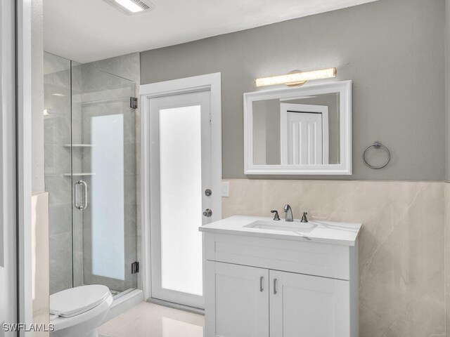 bathroom featuring vanity, a shower with shower door, tile walls, and toilet