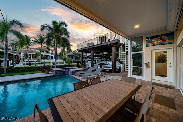 pool at dusk featuring an in ground hot tub and a patio