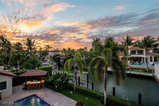 pool at dusk featuring a water view, exterior bar, and a patio area