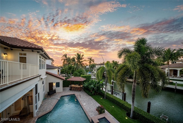 pool at dusk with a patio, a water view, and a bar