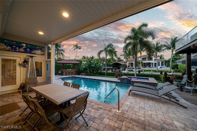 pool at dusk with an in ground hot tub and a patio