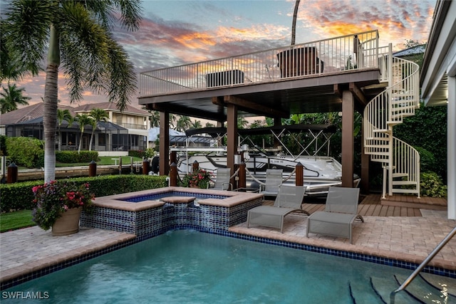 pool at dusk featuring a patio area and an in ground hot tub