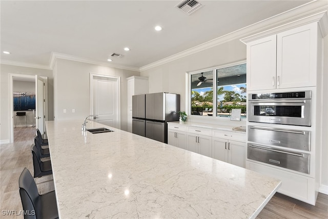 kitchen with appliances with stainless steel finishes, a kitchen breakfast bar, light stone counters, sink, and white cabinets