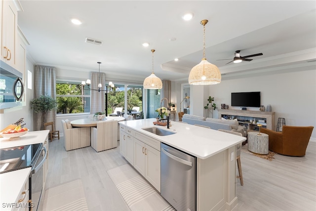 kitchen with appliances with stainless steel finishes, a kitchen island with sink, sink, white cabinets, and hanging light fixtures