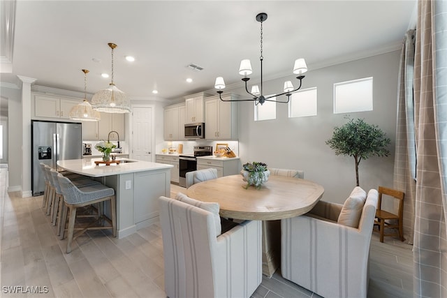 dining room featuring a notable chandelier, sink, crown molding, and light hardwood / wood-style flooring