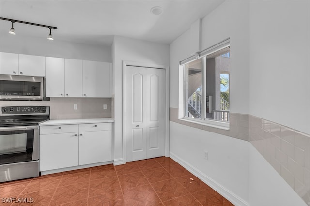 kitchen with track lighting, white cabinets, appliances with stainless steel finishes, and tile patterned floors