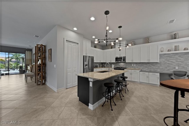 kitchen featuring white cabinetry, an island with sink, stainless steel appliances, and light stone counters