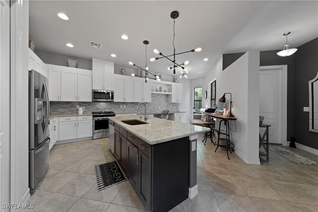 kitchen featuring sink, light stone counters, an island with sink, white cabinets, and appliances with stainless steel finishes