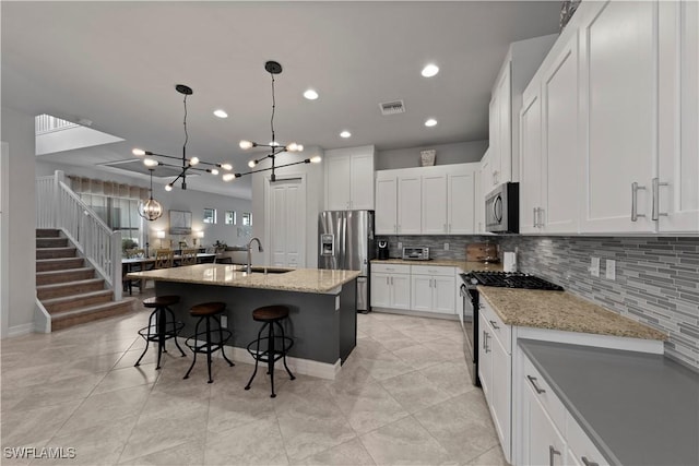 kitchen featuring light stone countertops, backsplash, stainless steel appliances, white cabinetry, and an island with sink